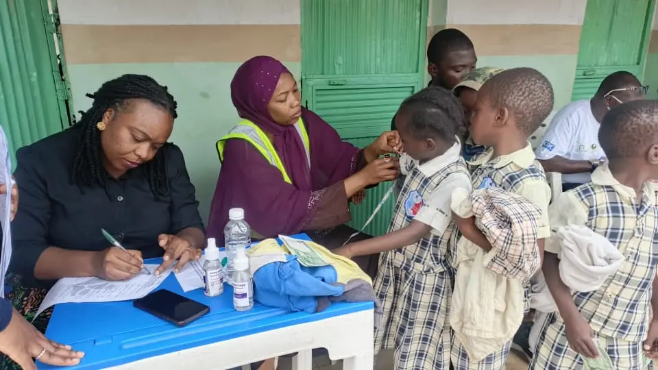 A TB testing officer measuring and noting the height and weight of the children.